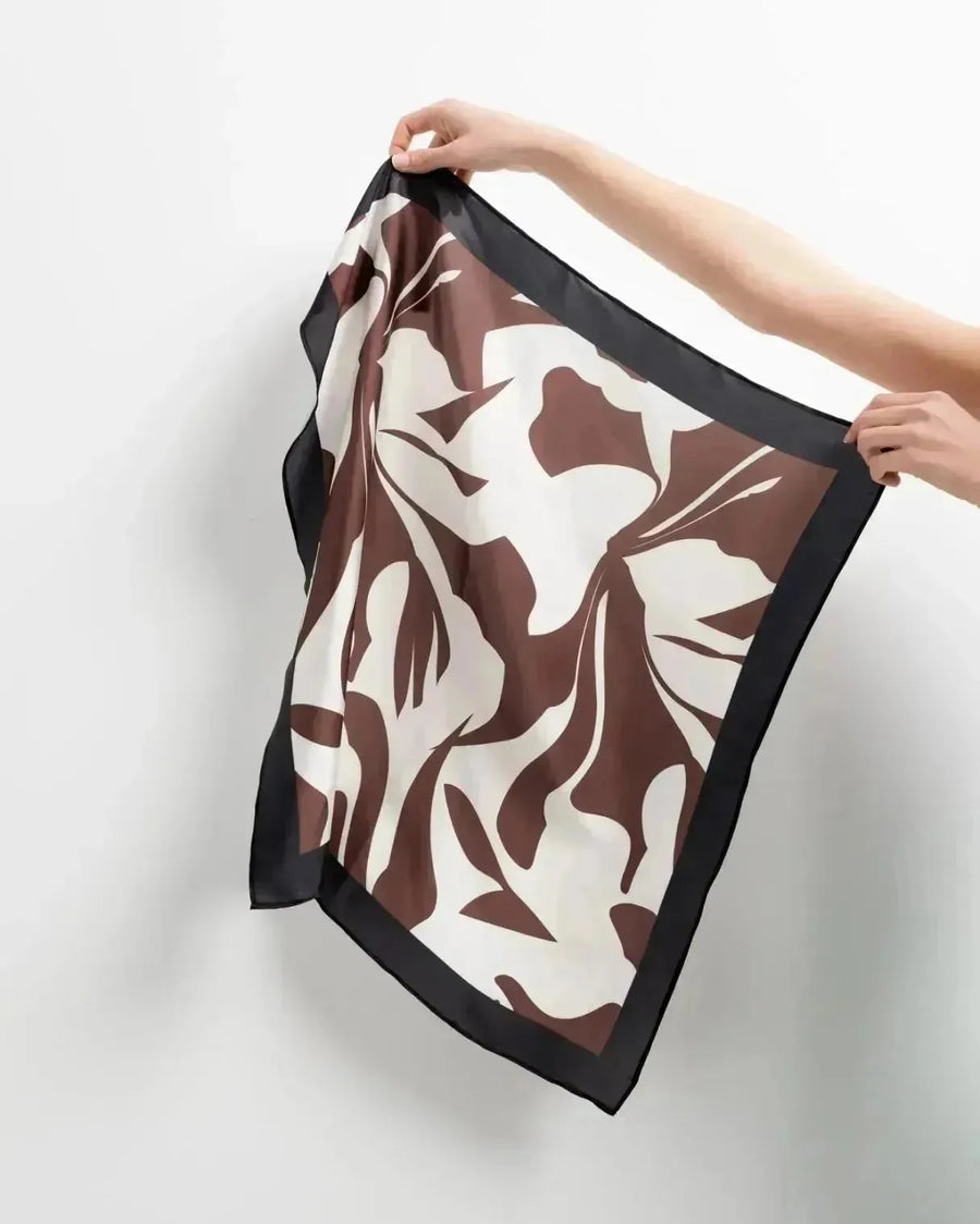 Foulard femme carré imprimé floral marron et blanc cassé tenu à la main, mettant en valeur le design élégant de cet accessoire.