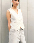 Femme portant un gilet blanc sans manches chic coupe tailleur, avec des boutons ton sur ton, associé à un jean délavé.