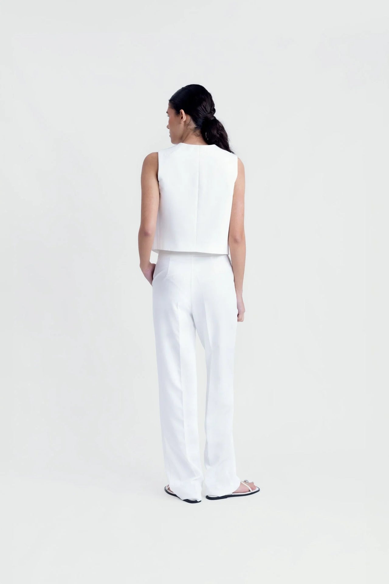 Vue arrière d'une femme dans un gilet sans manches chic, blanc, avec pantalon assorti, montrant la coupe tailleur élégante.