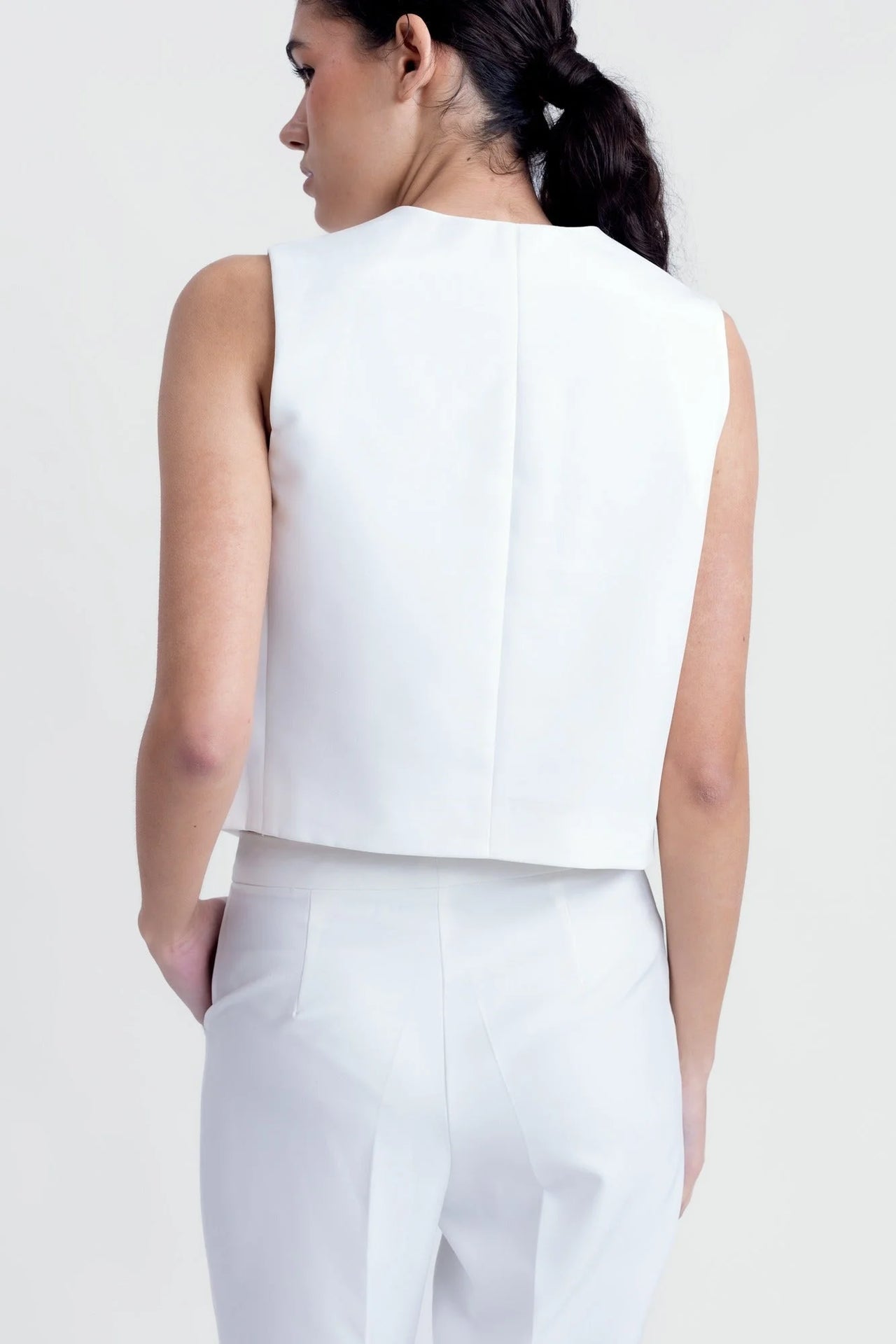 Détail du dos d'une femme dans un gilet sans manches chic blanc, style tailleur, sur un fond neutre.