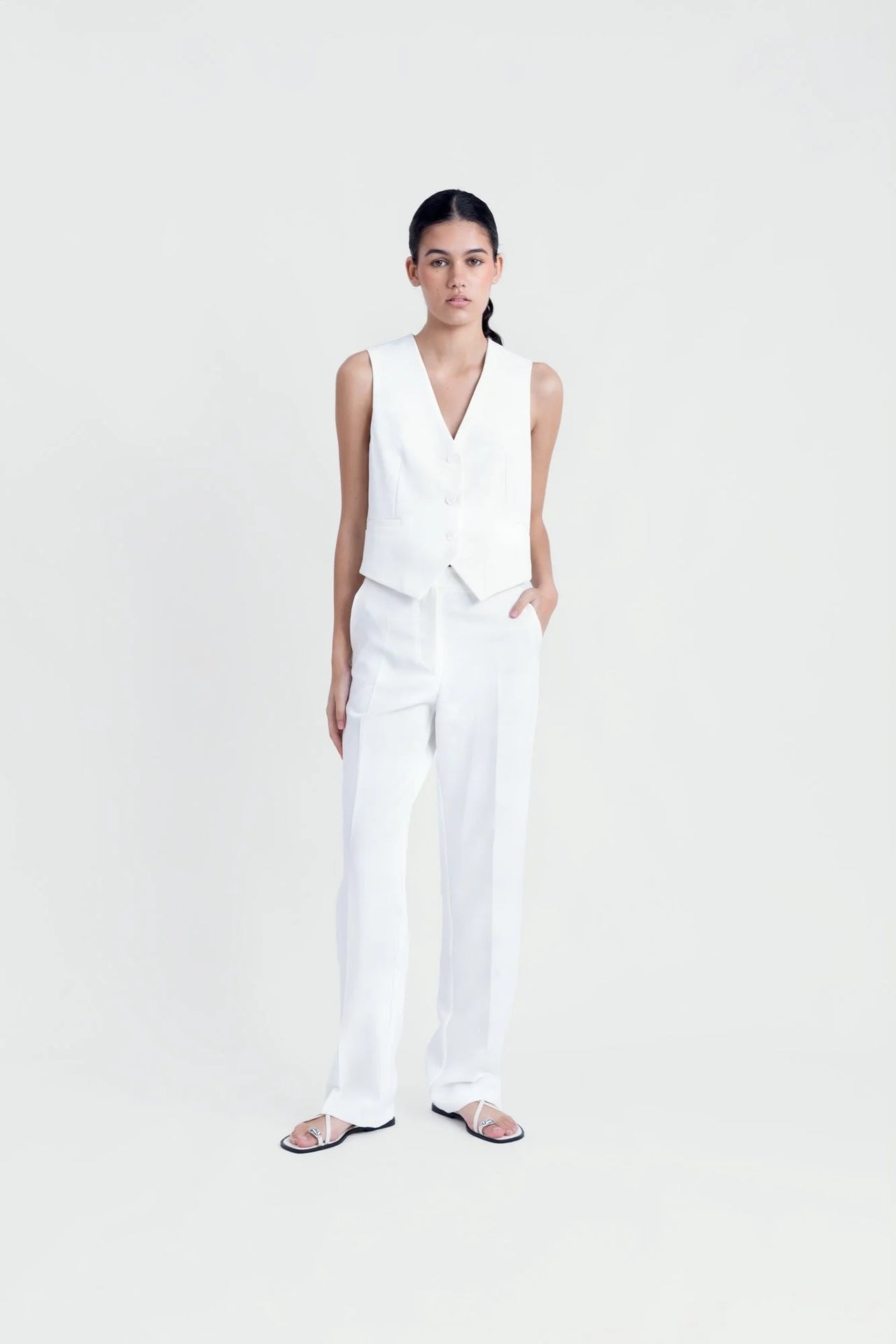Femme posant en gilet sans manches chic, blanc et élégant, avec pantalon assorti, pour un look tendance.