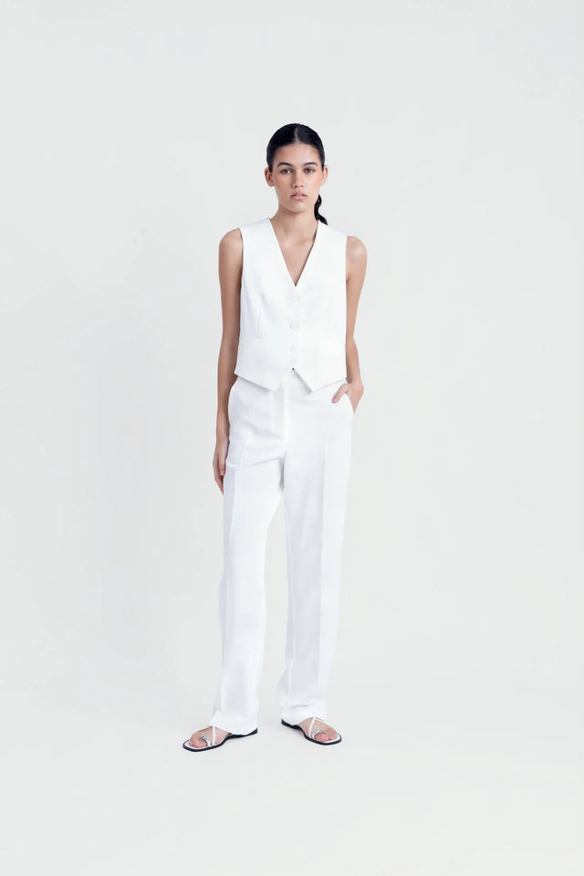 Femme posant en gilet sans manches chic, blanc et élégant, avec pantalon assorti, pour un look tendance.