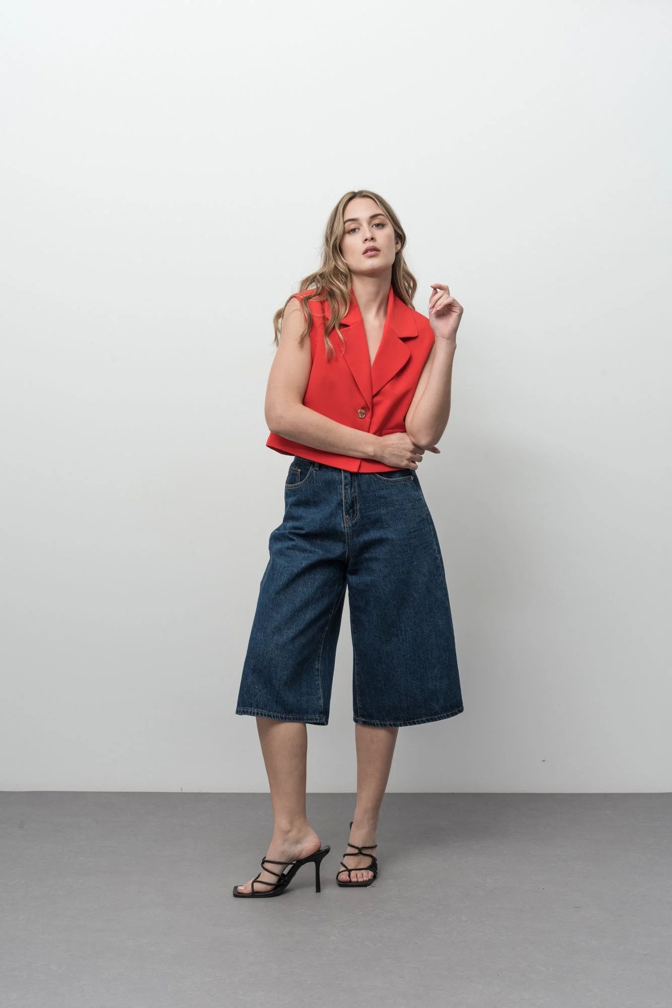 Modèle portant un gilet court sans manches blanc cassé et rouge vif avec culottes en denim foncé et talons noirs