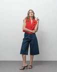 Modèle portant un gilet court sans manches blanc cassé et rouge vif avec culottes en denim foncé et talons noirs