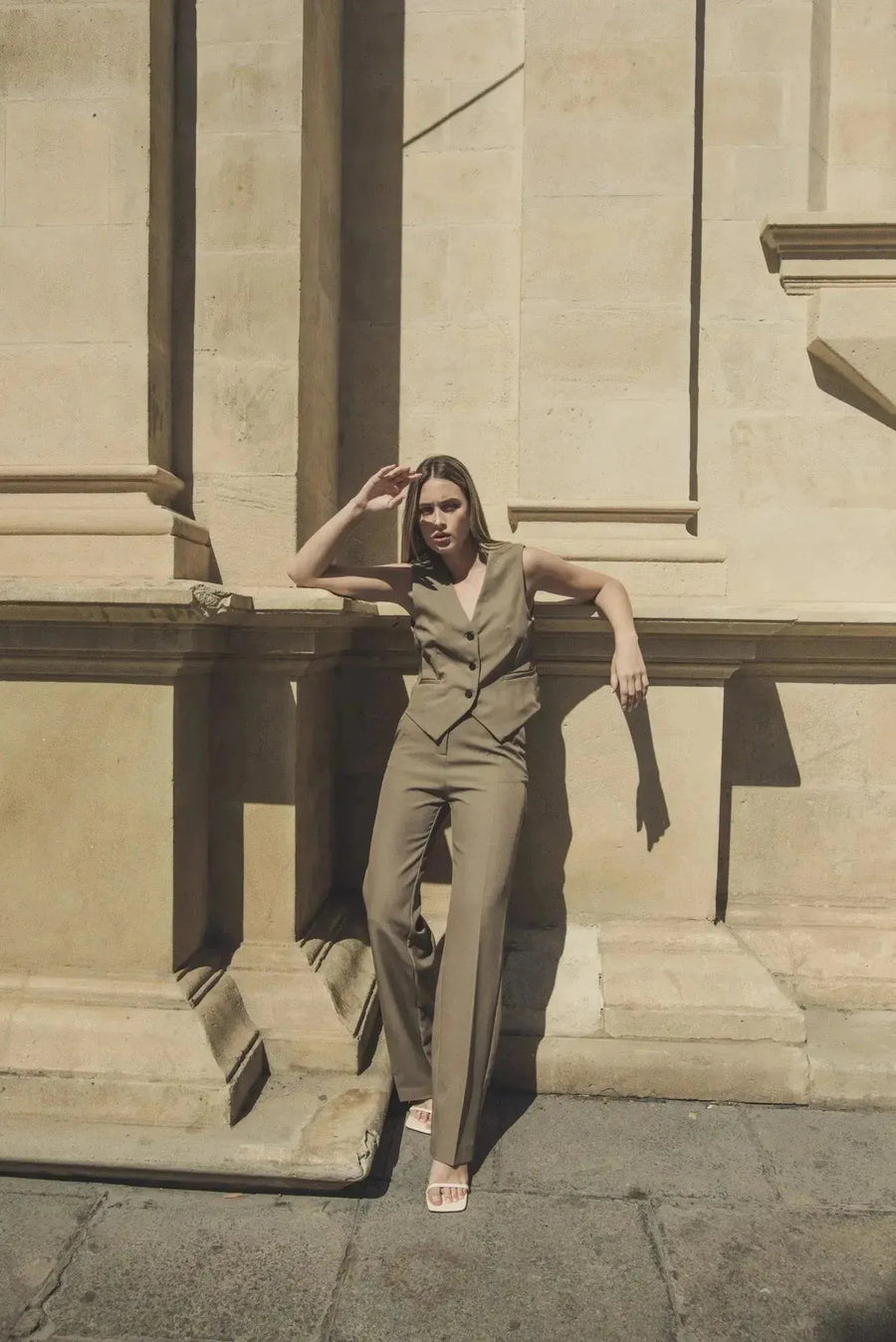 Modèle extérieur d'une femme dans un gilet élégant vert facile à assortir, un gilet court sans manche femme, avec un pantalon assorti devant une architecture.