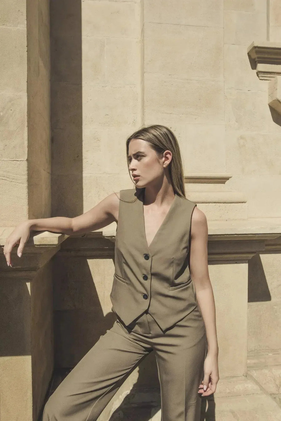 Femme stylée dans un gilet élégant vert facile à assortir, un gilet court sans manche femme, prenant la pose près d'une colonne avec un style sophistiqué.