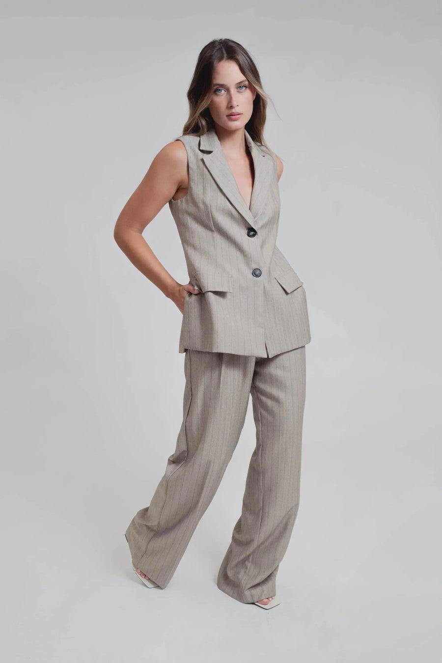 Modèle posant fièrement dans un gilet sans manches femme chic à rayures fines élégant et pantalon assorti, incarnant le style moderne. Gilet costume femme pour un style polyvalent.