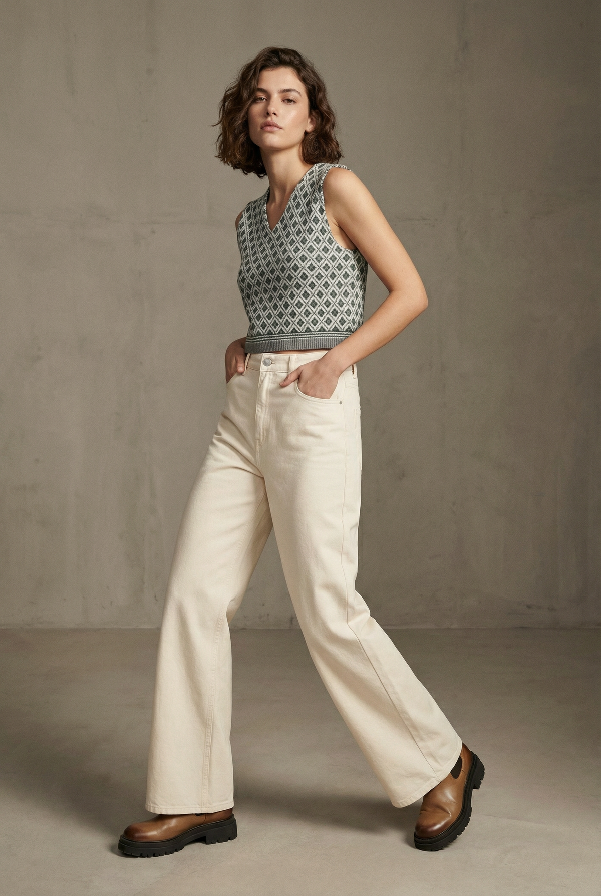 Gilet sans manches gris à motifs losanges, porté avec un pantalon écru, pose en mouvement