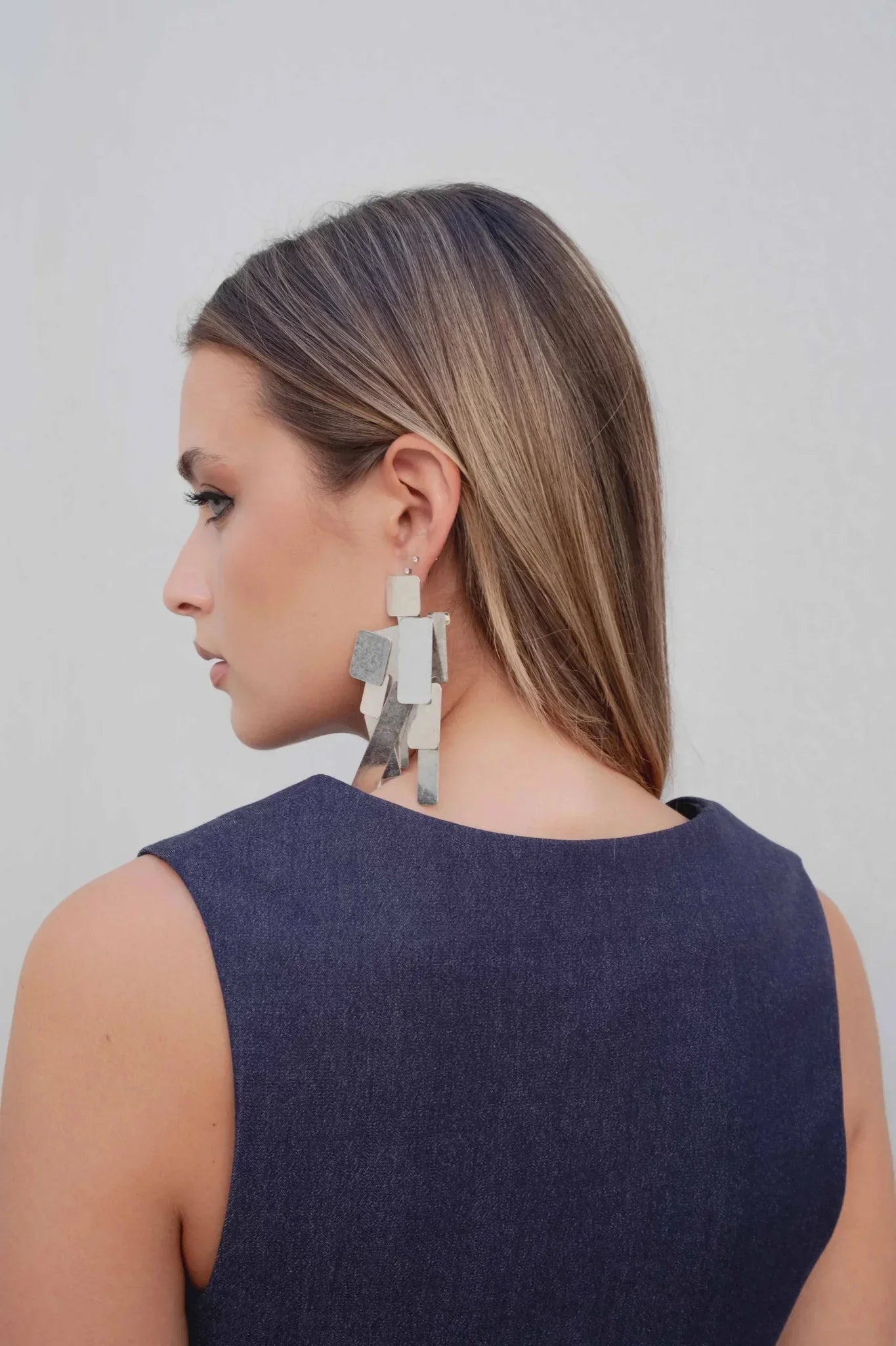 Femme portant un gilet court bleu indigo et une boucle d’oreille géométrique claire