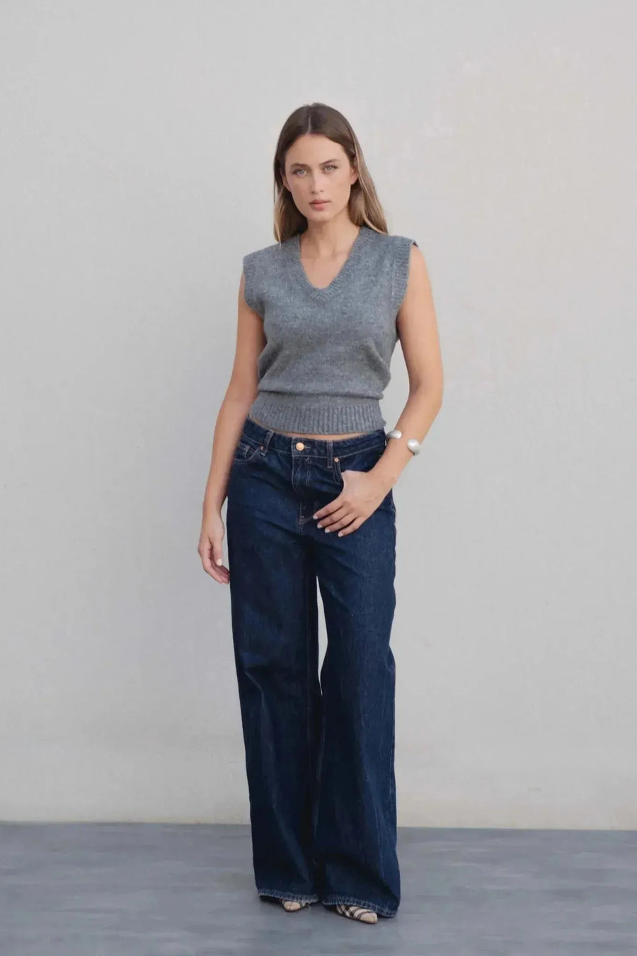 Modèle portant un gilet tricoté femme col V gris associé à un jean, illustrant un look tendance. Ce gilet tricot sans manche femme est polyvalent pour toutes les occasions.