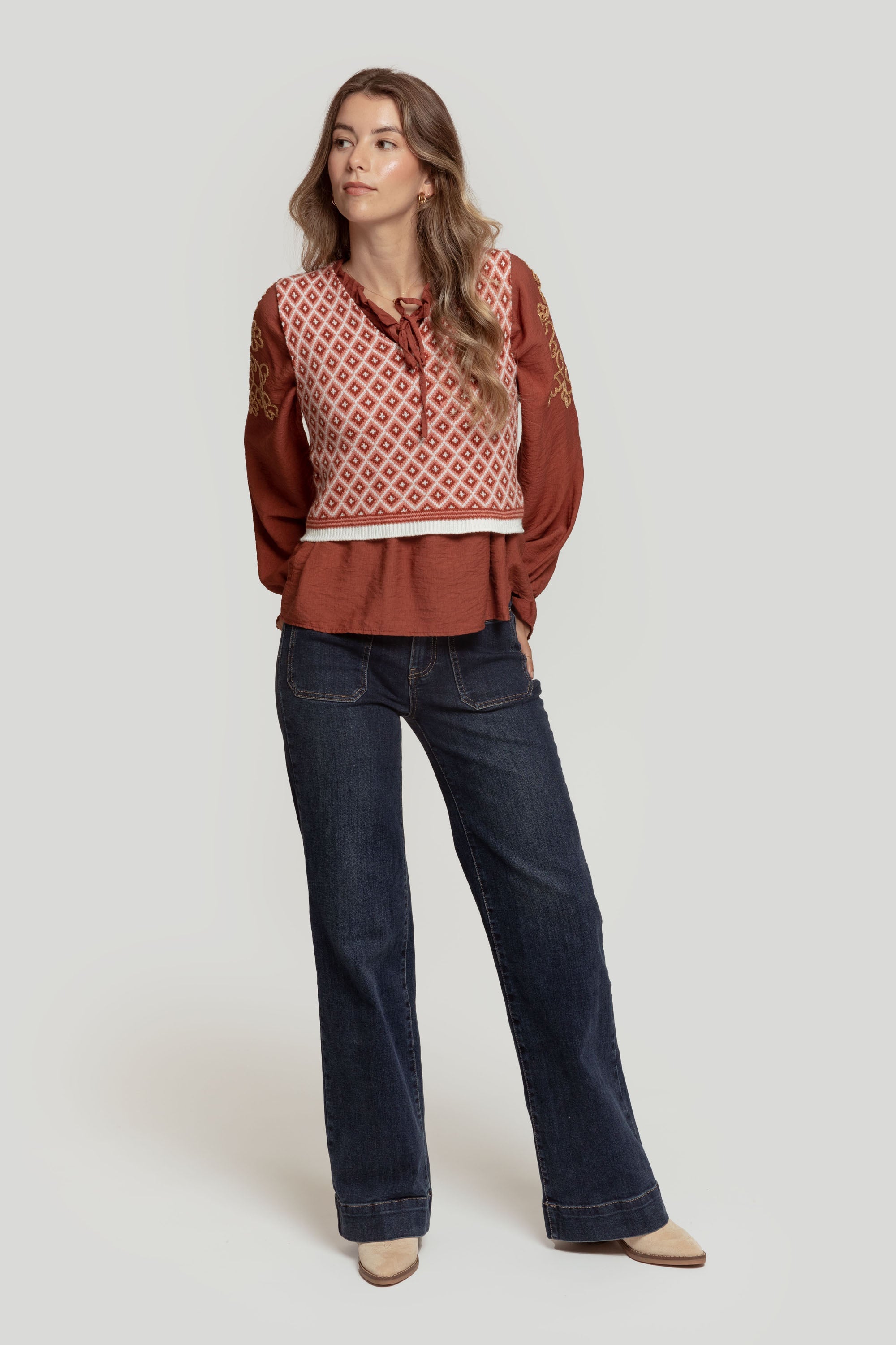 Femme stylée dans un gilet femme en maille sans manches géométrique, superposé à un top rouge, avec un pantalon en denim.