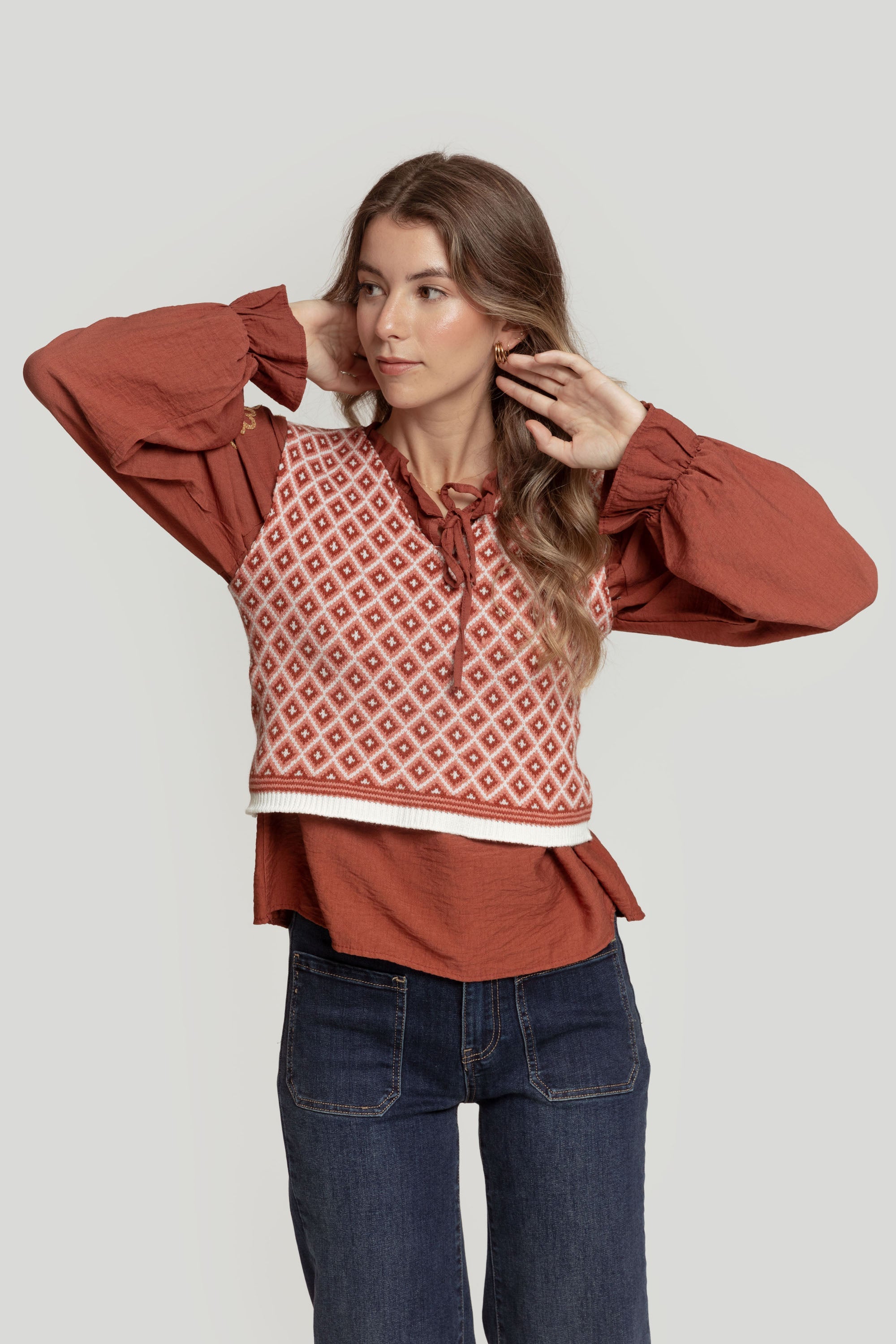 Modèle en gilet femme en maille sans manches géométrique, pose avec élégance, combinaison d'un haut rouge et bas en jean.