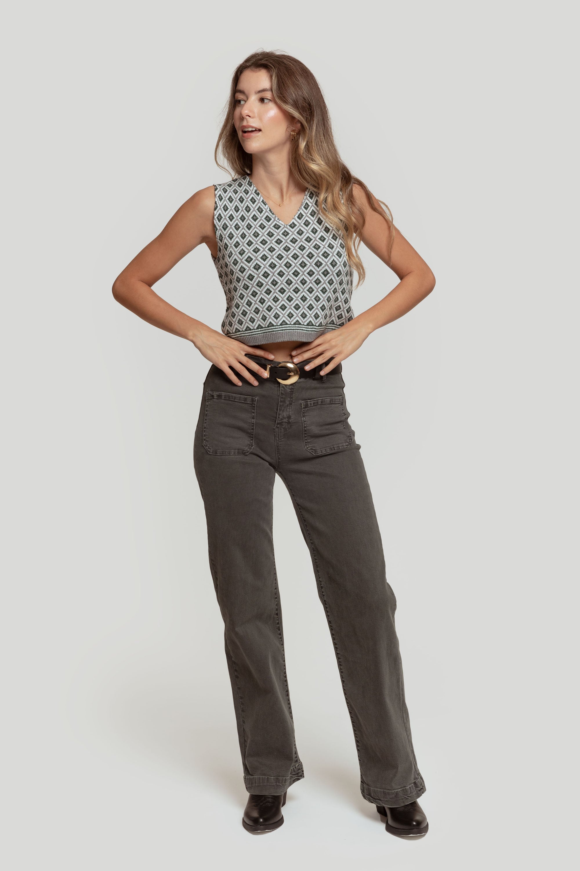 Modèle portant un gilet femme en maille sans manches géométrique, associé à un pantalon gris, affichant une pose décontractée.