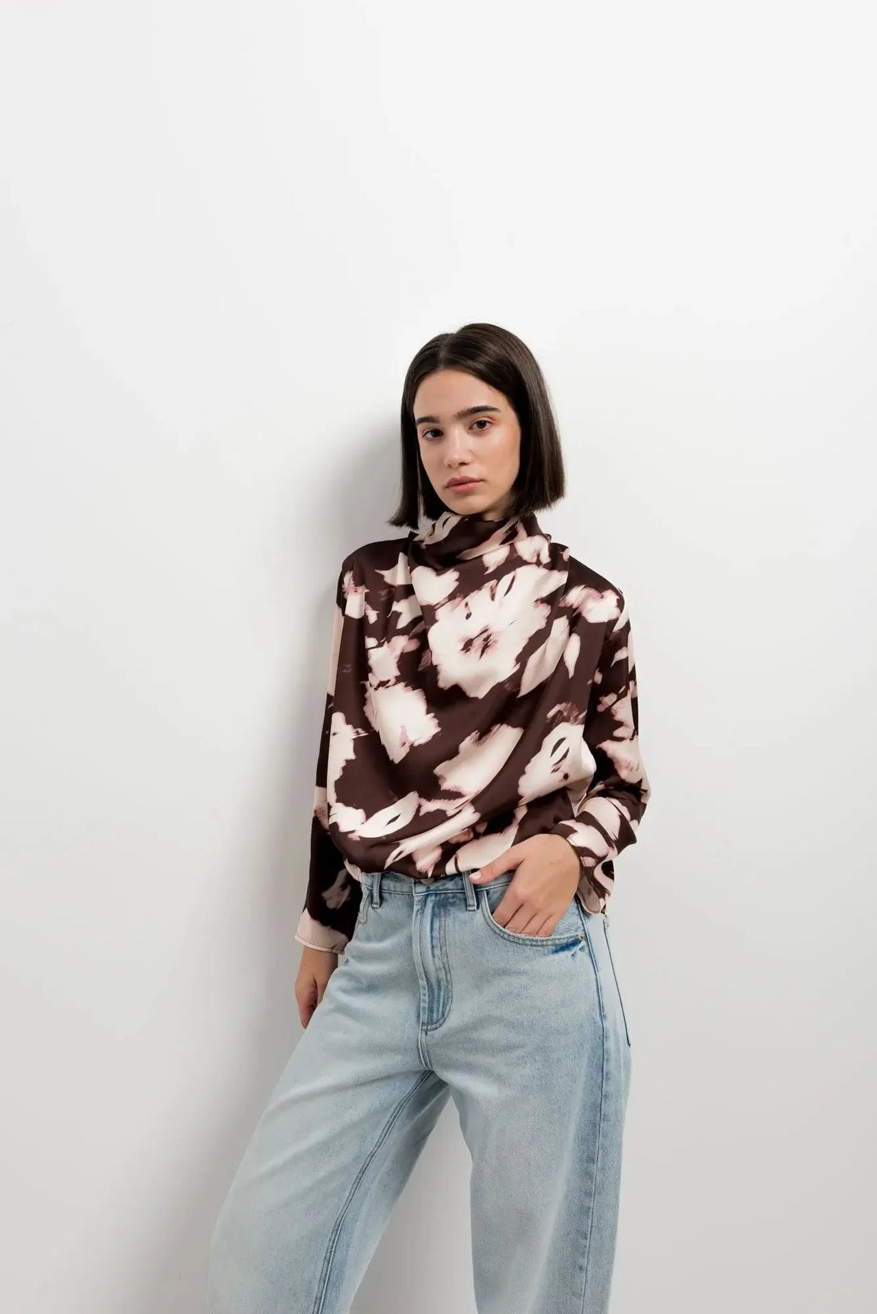 Modèle posant dans un studio avec la blouse femme à col bénitier et imprimé abstrait, combinée avec un jean, pour un look actuel.