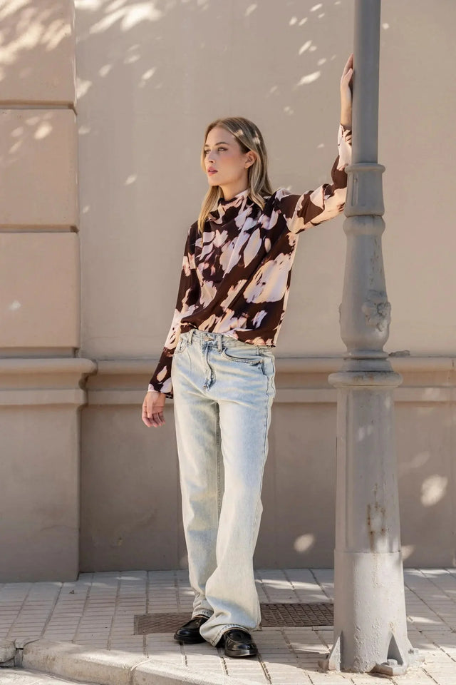 Modèle posant élégamment avec la blouse femme à col bénitier et imprimé abstrait, associée à un jean décontracté.