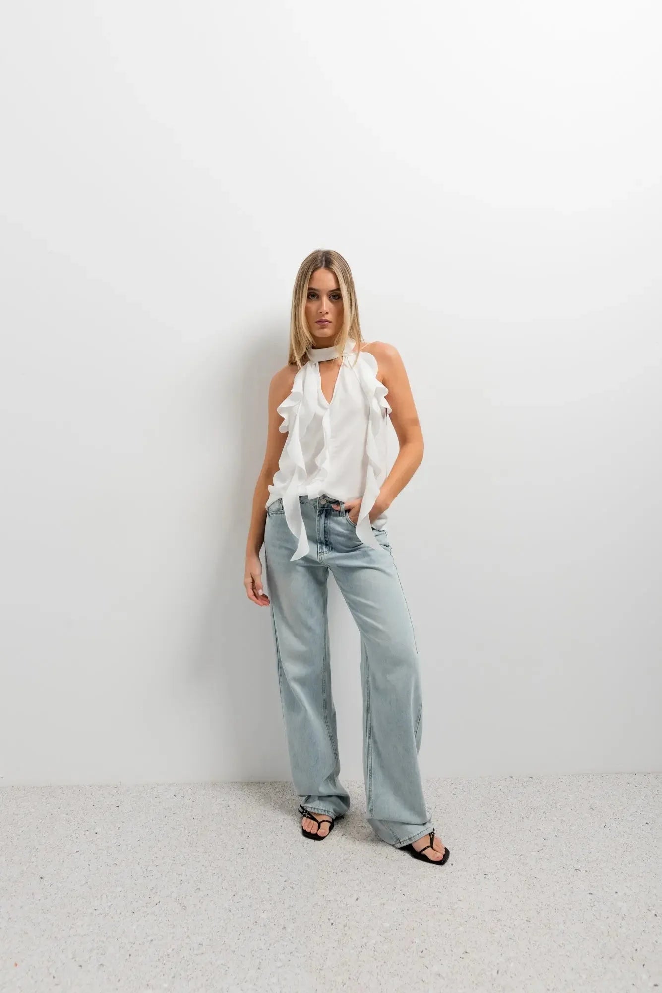 Haut à volants femme chic en tissu lisse, modèle stylé avec jean, posé dans un cadre minimaliste.