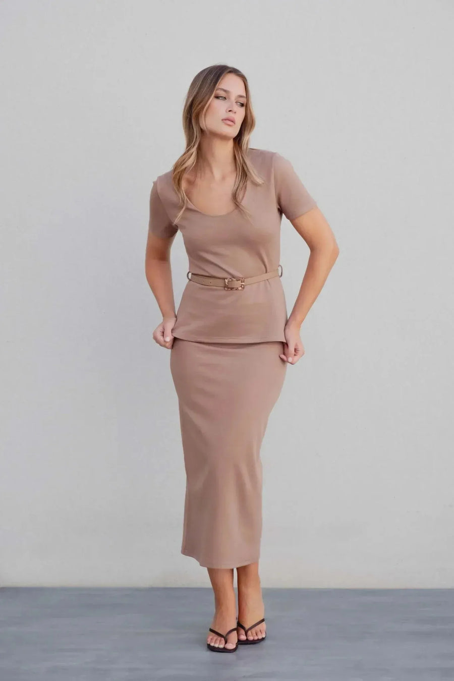 Femme souriante en haut chic femme taupe et jupe, en pleine pose, pour une allure moderne et stylée.