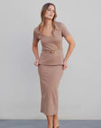 Femme souriante en haut chic femme taupe et jupe, en pleine pose, pour une allure moderne et stylée.