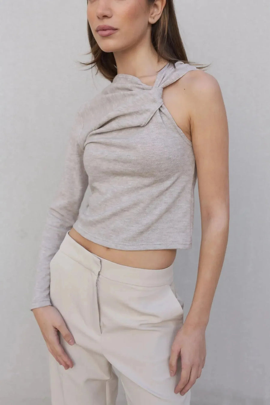 Haut asymétrique femme beige clair à une épaule, présenté de près avec une pose qui souligne le confort et l'élégance.