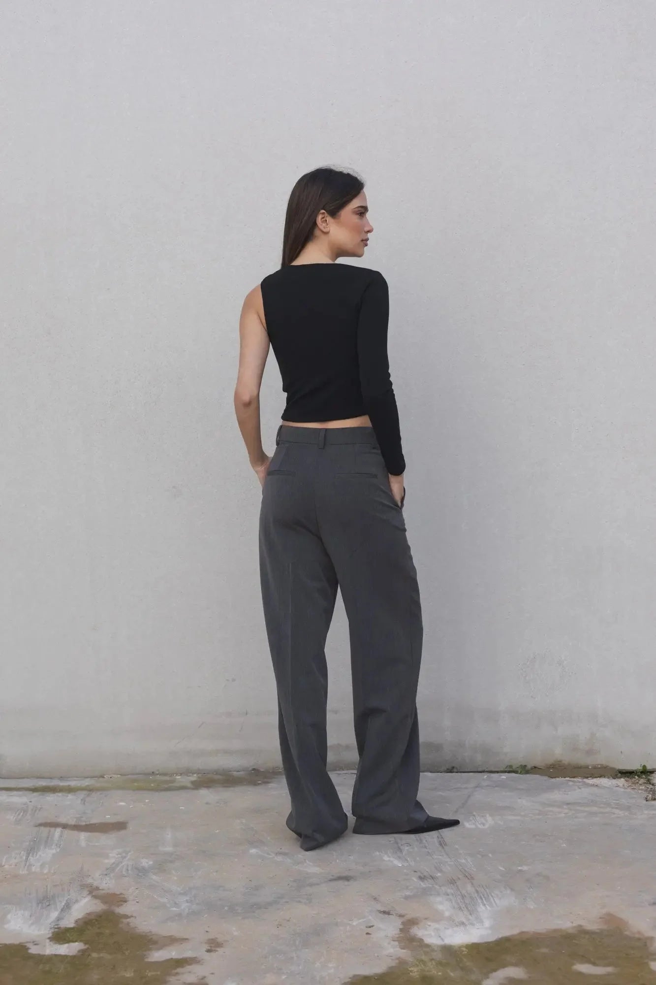 Femme portant un haut asymétrique beige clair à une épaule et pantalon large gris foncé