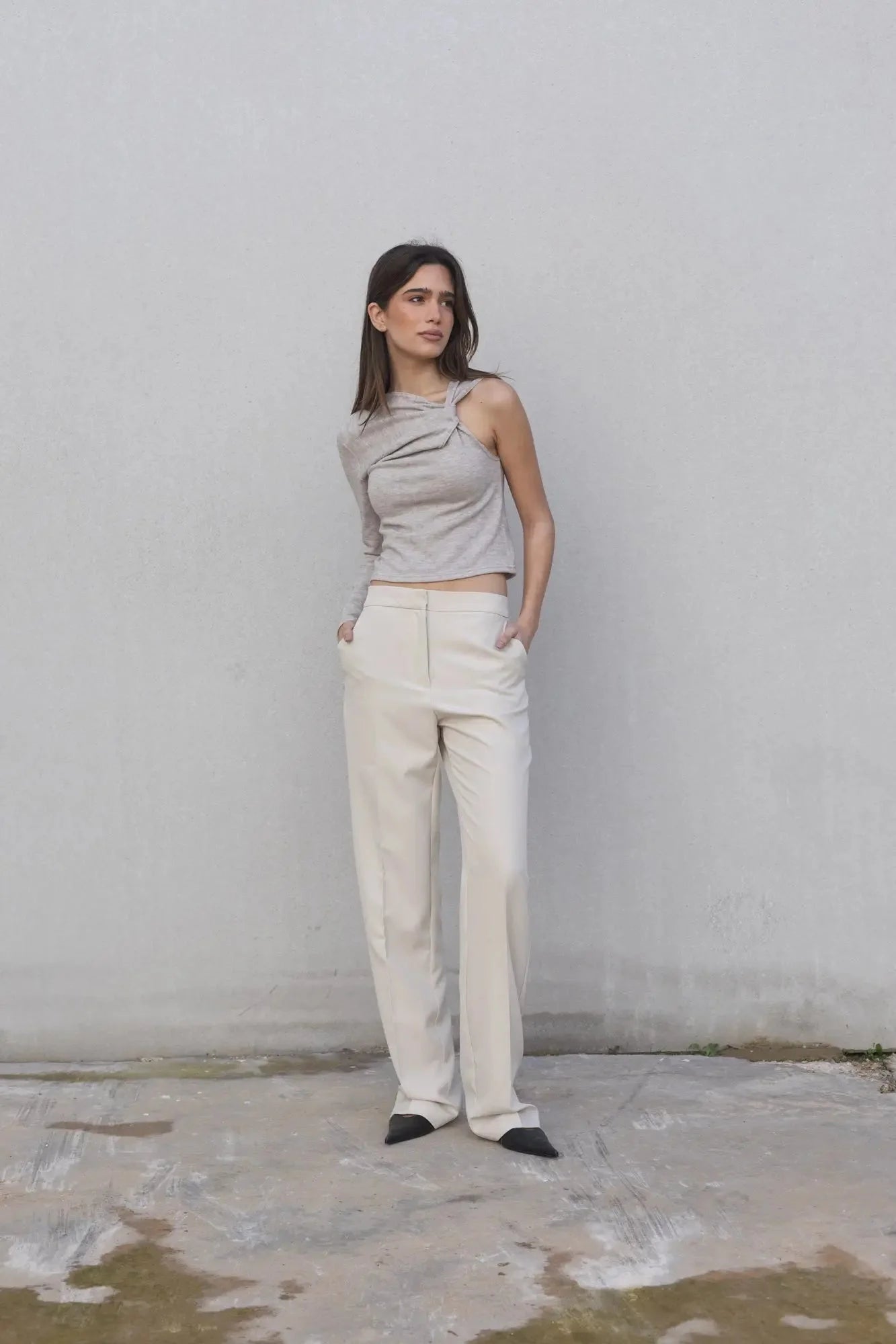 Femme portant un haut asymétrique beige clair à une épaule et un pantalon crème