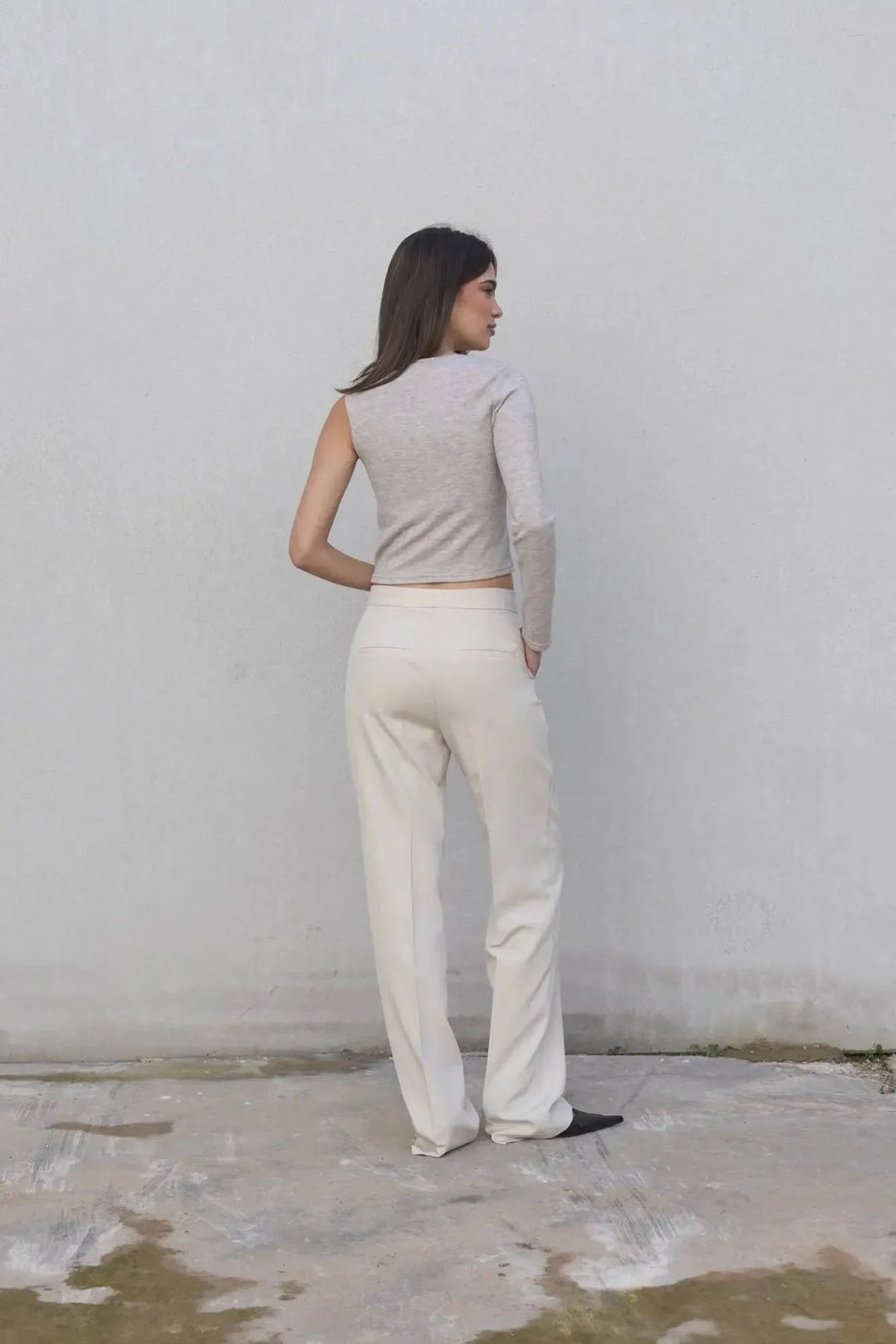 Vue arrière du haut asymétrique femme beige clair à une épaule, associé à un pantalon blanc pour un style chic.