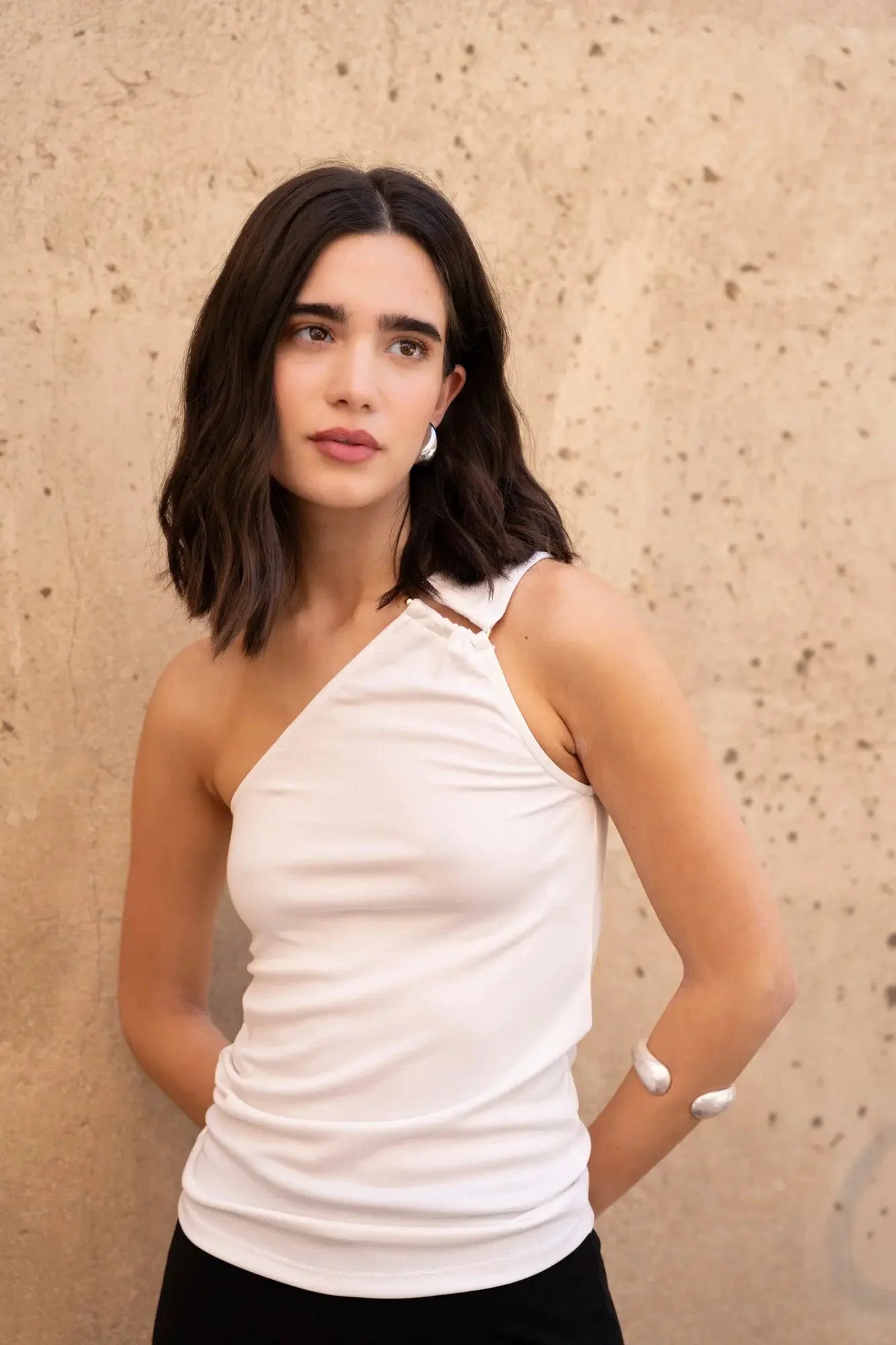 Modèle portant un haut asymétrique blanc avec boucle, parfait pour ajouter une touche d'élégance chic pour toutes les occasions.