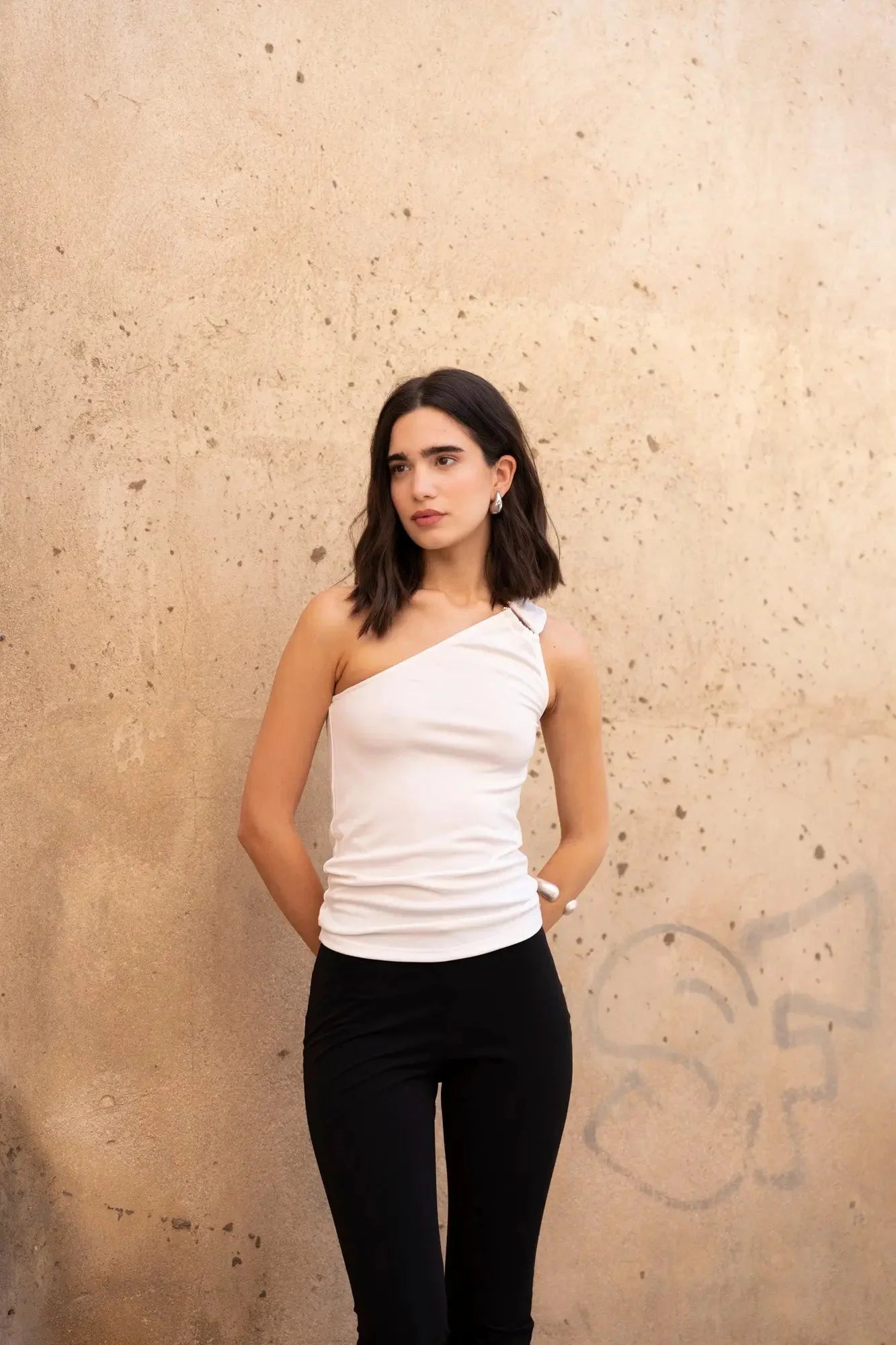 Femme posant avec un haut asymétrique blanc, un choix parfait pour toutes les occasions élégantes et décontractées.