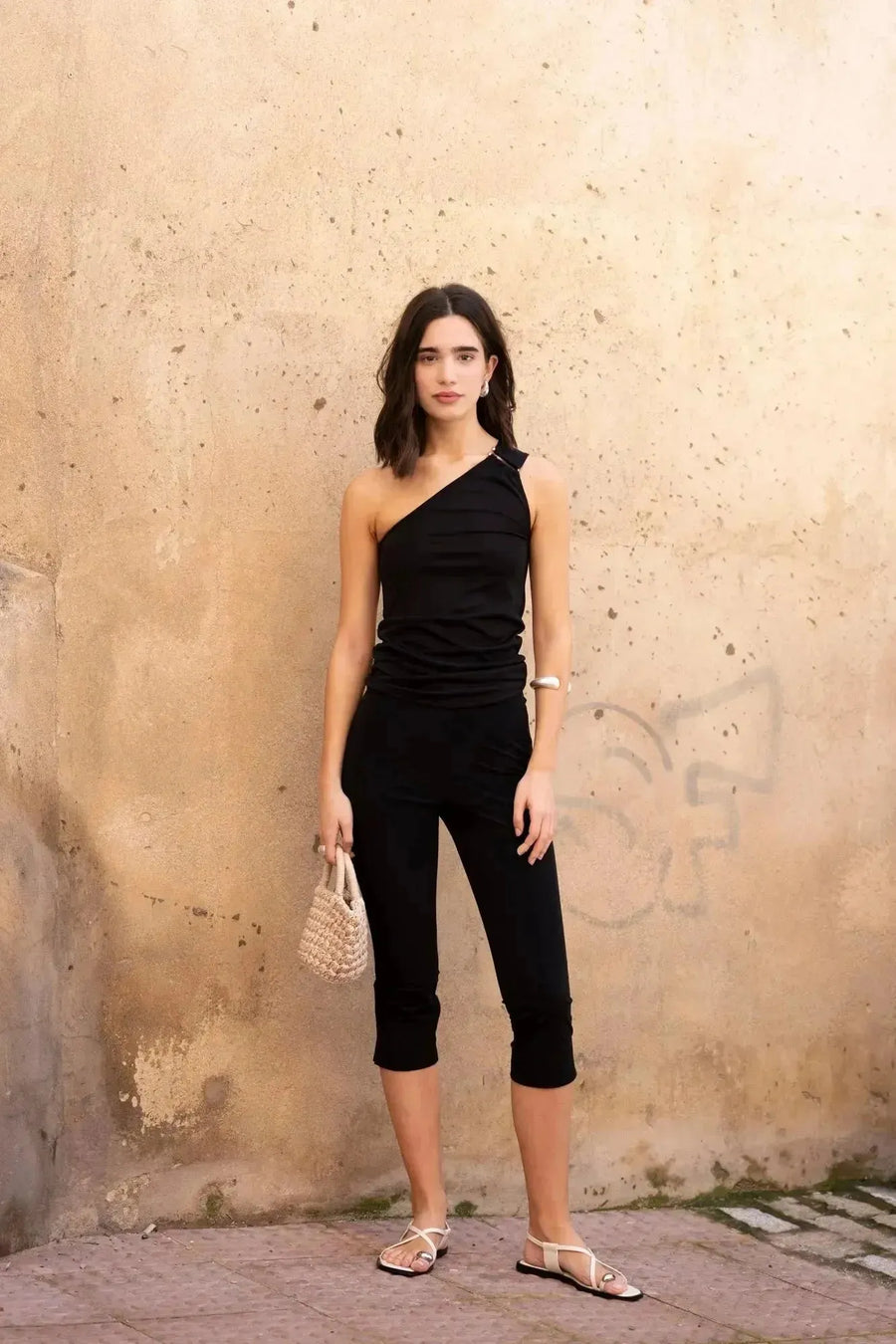 Femme avec un haut asymétrique noir sur fond de mur, un style chic pour des sorties.
