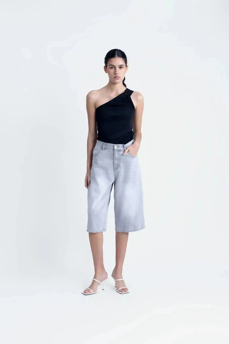 Modèle dans un haut asymétrique noir, mettant en valeur une tenue style décontracté avec une touche d'élégance.