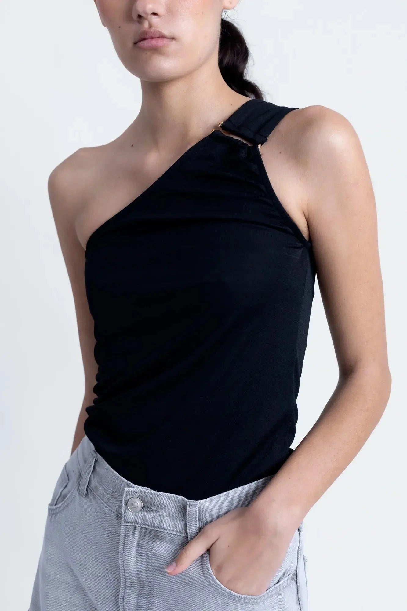 Femme en gros plan dans un haut asymétrique noir, mettant en avant son design moderne et chic.