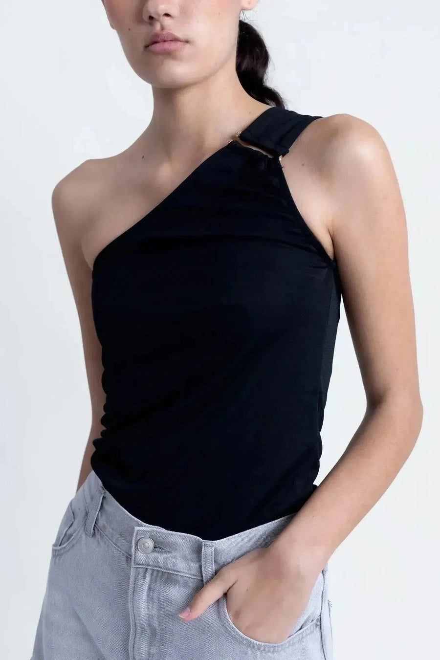 Femme en gros plan dans un haut asymétrique noir, mettant en avant son design moderne et chic.