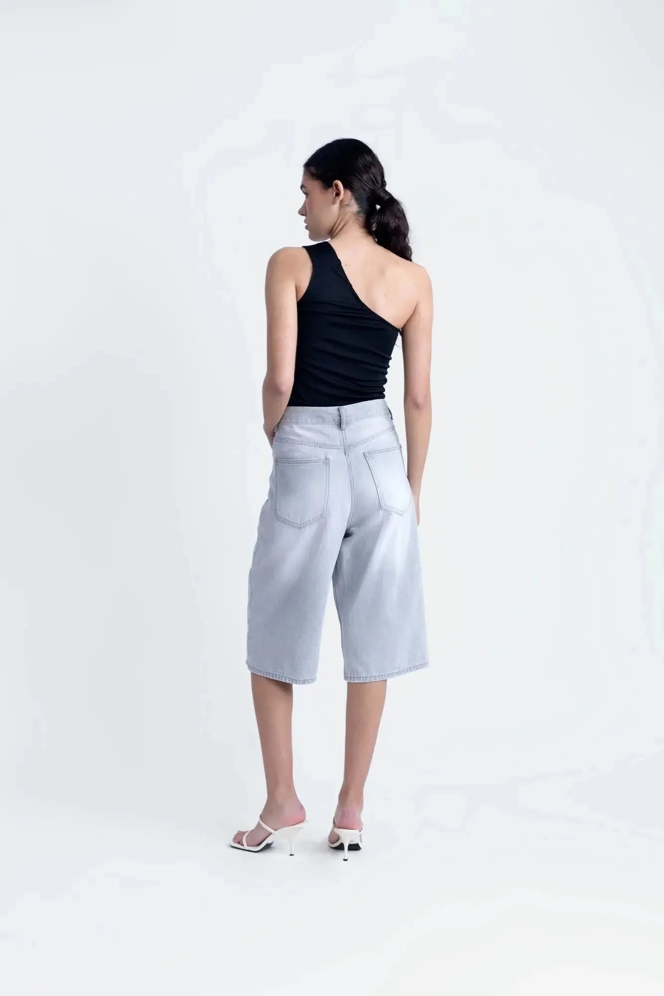 Femme en haut asymétrique noir, affichant une allure décontractée et à la mode avec un jean.