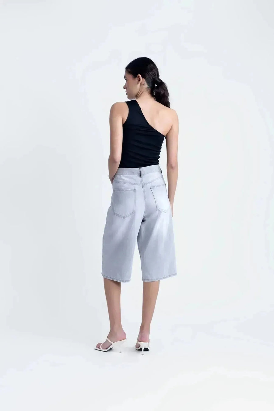 Femme en haut asymétrique noir, affichant une allure décontractée et à la mode avec un jean.
