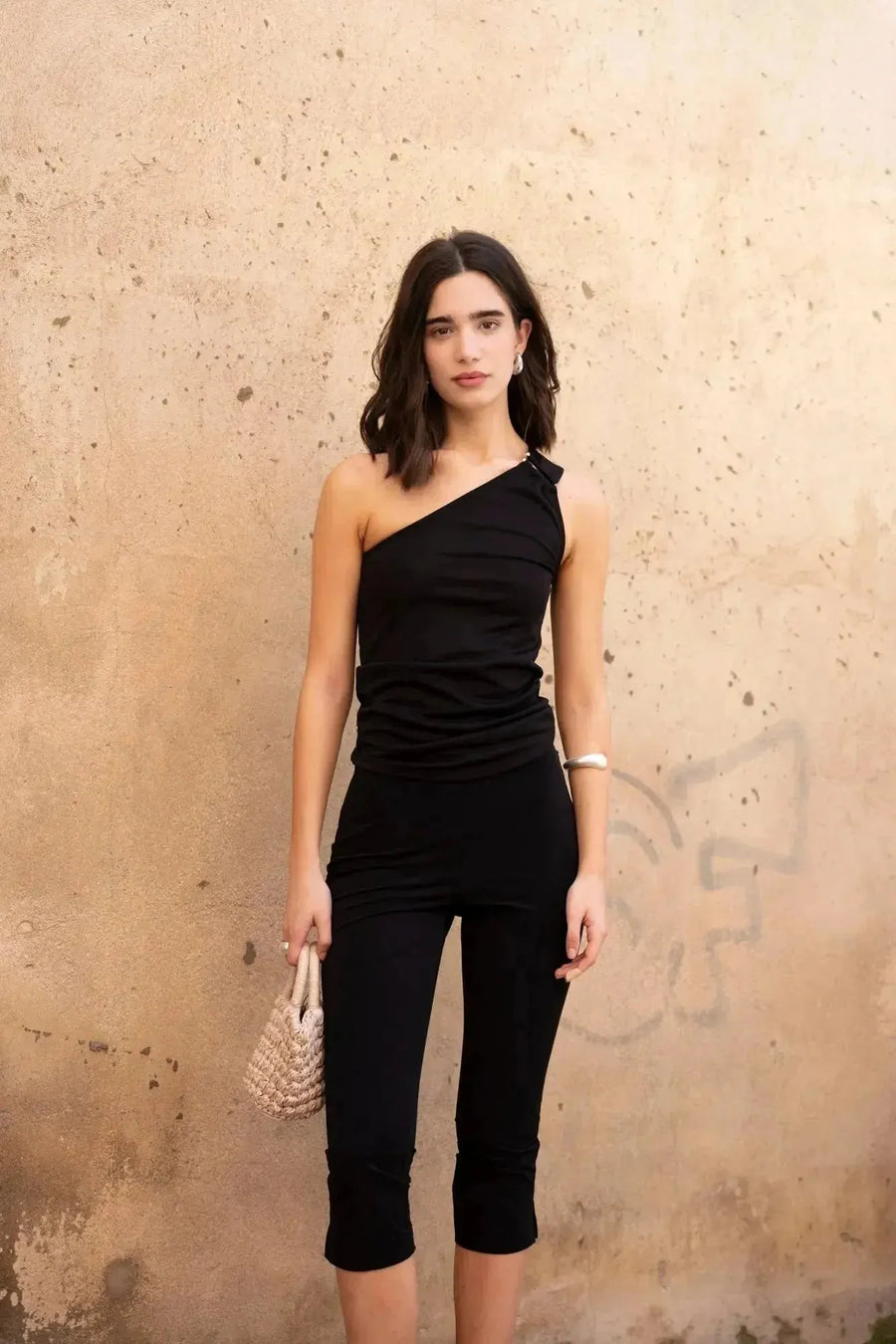 Modèle portant un haut asymétrique noir avec boucle dorée, une tenue élégante et polyvalente pour toutes occasions.