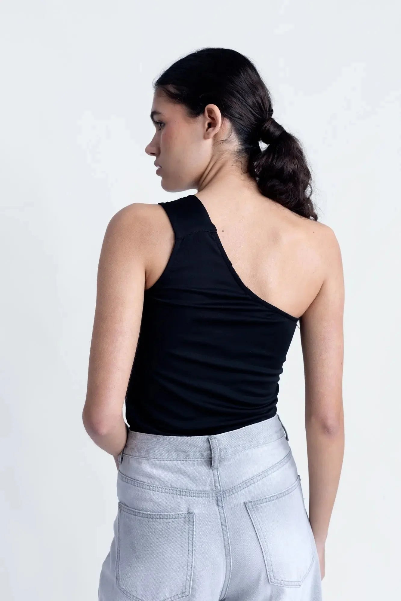 Vue arrière d'une femme portant un haut asymétrique noir, combiné à un look décontracté.