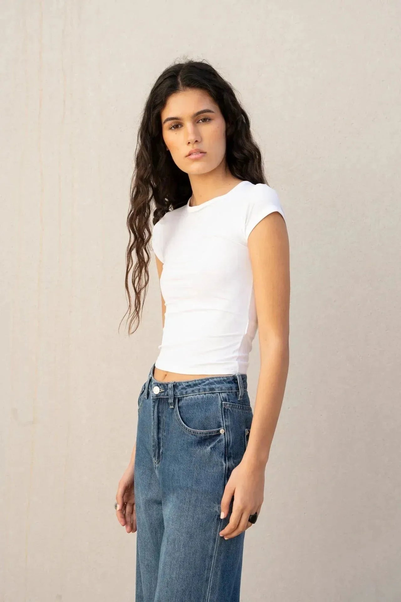 Détail d'une jeune femme vêtue d'un tee-shirt blanc, mettant en valeur son jean à jambe large et ourlets retroussés, parfait pour un look jean ample femme.