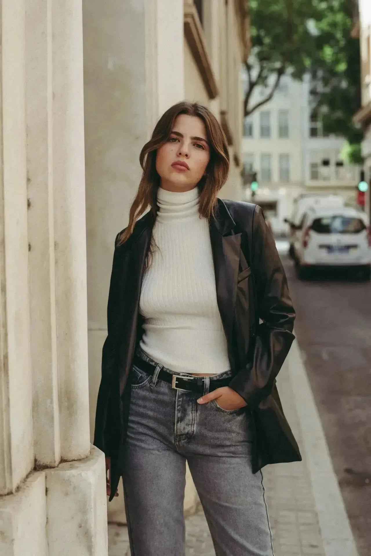 Femme posant dans un jean femme taille haute droit gris et un pull, avec une veste en cuir pour un style chic.