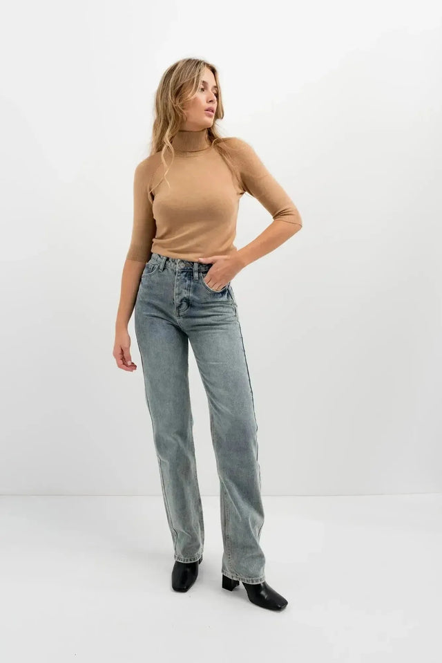 Femme en jean femme taille haute droit gris et pull marron, affichant une pose élégante devant un fond neutre.