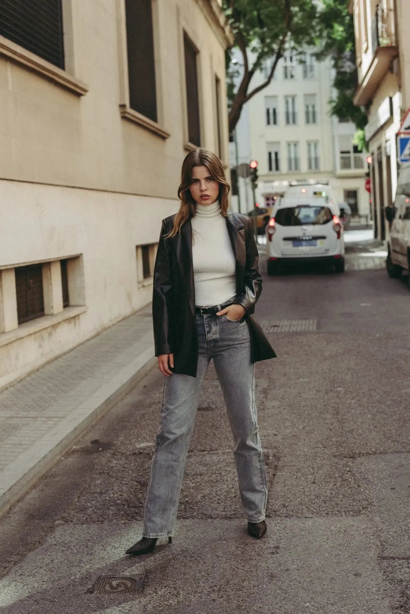 Jeans taille haute coupe droite portés par une femme en blazer en cuir noir et turtleneck blanc