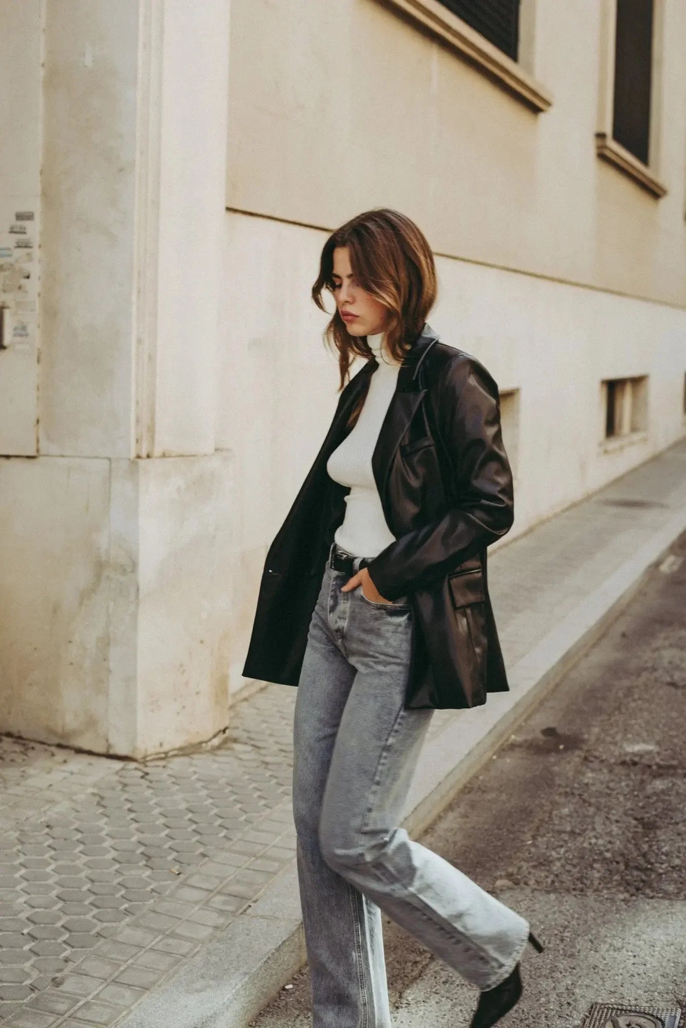 Femme portant un blazer en cuir noir, turtleneck blanc et jeans taille haute coupe droite