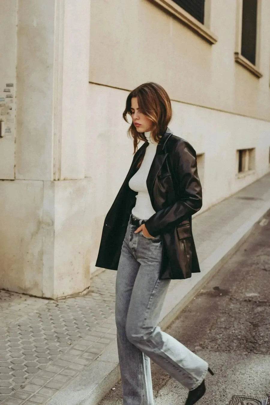 Femme élégante en jean femme taille haute droit gris, marchant dans la rue avec une veste en cuir, look décontracté.