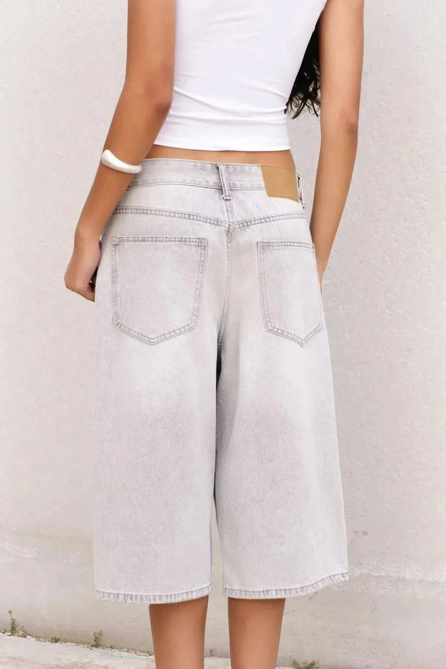 Arrière d'une femme posant en bermuda jean femme gris clair, mettant en valeur son style décontracté et contemporain.