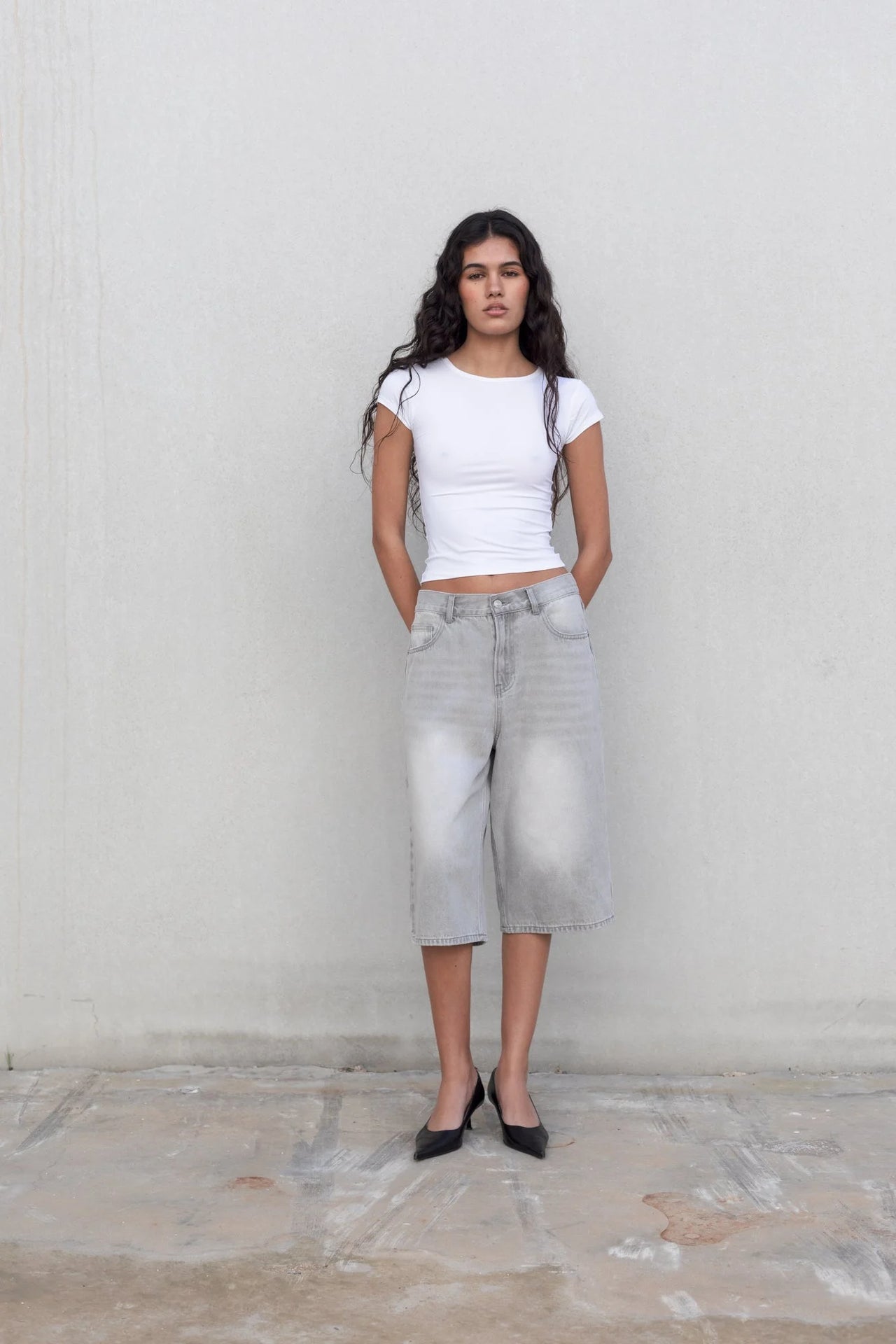 Femme posant avec style en bermuda jean femme gris clair, oversize et à taille haute, associé à un t-shirt blanc, parfait pour un look décontracté.