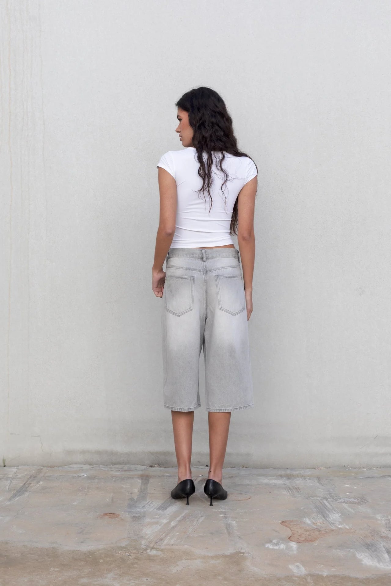 Vue arrière d'une femme en bermuda jean femme gris clair, mettant en avant la coupe large et la taille haute, portée avec un t-shirt.