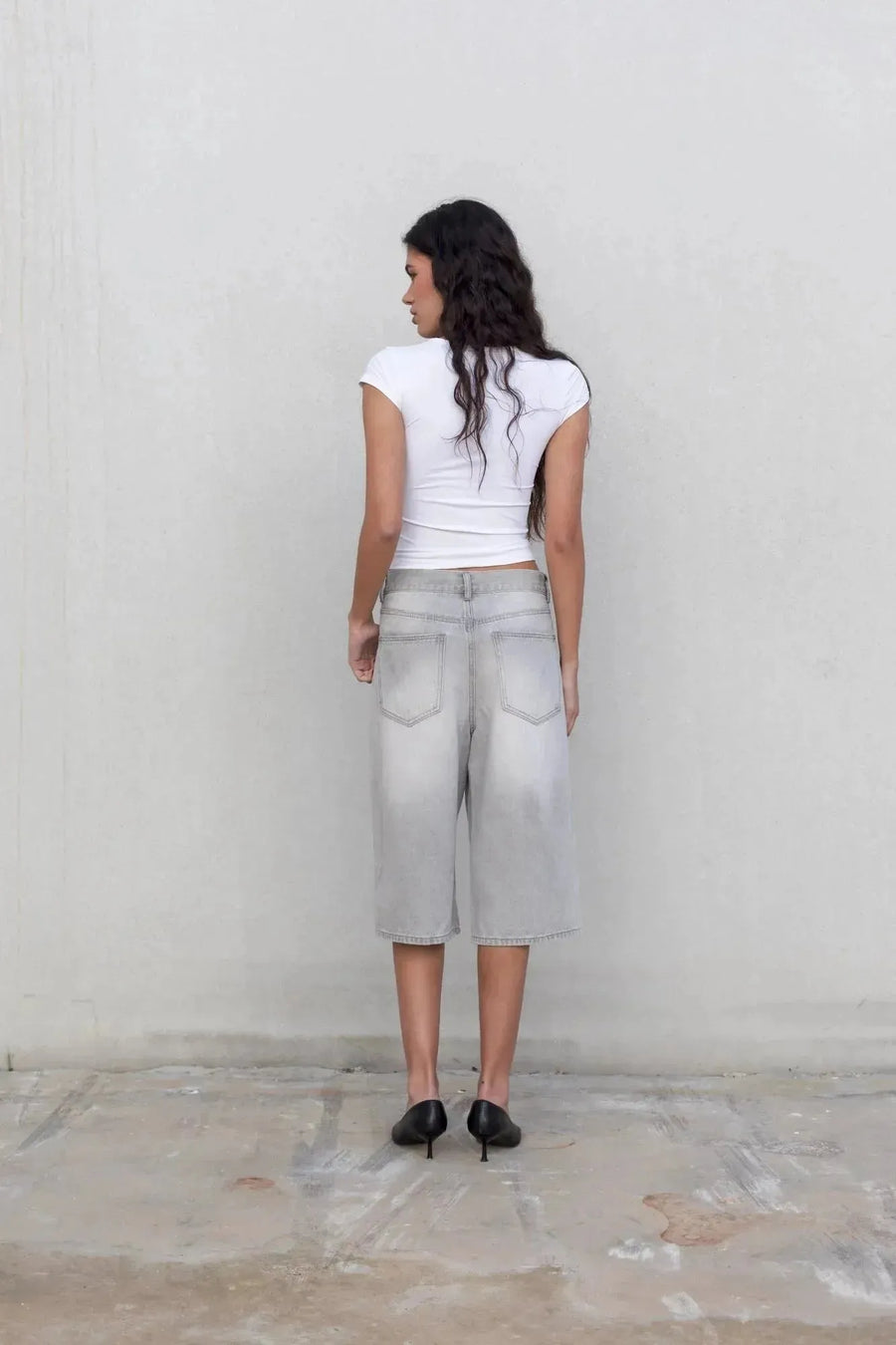 Vue arrière d'une femme en bermuda jean femme gris clair, mettant en avant la coupe large et la taille haute, portée avec un t-shirt.