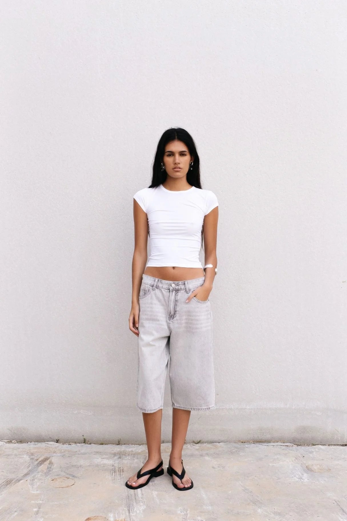 Femme portant un top blanc coupe large pour jean gris bermuda oversize et flip-flops