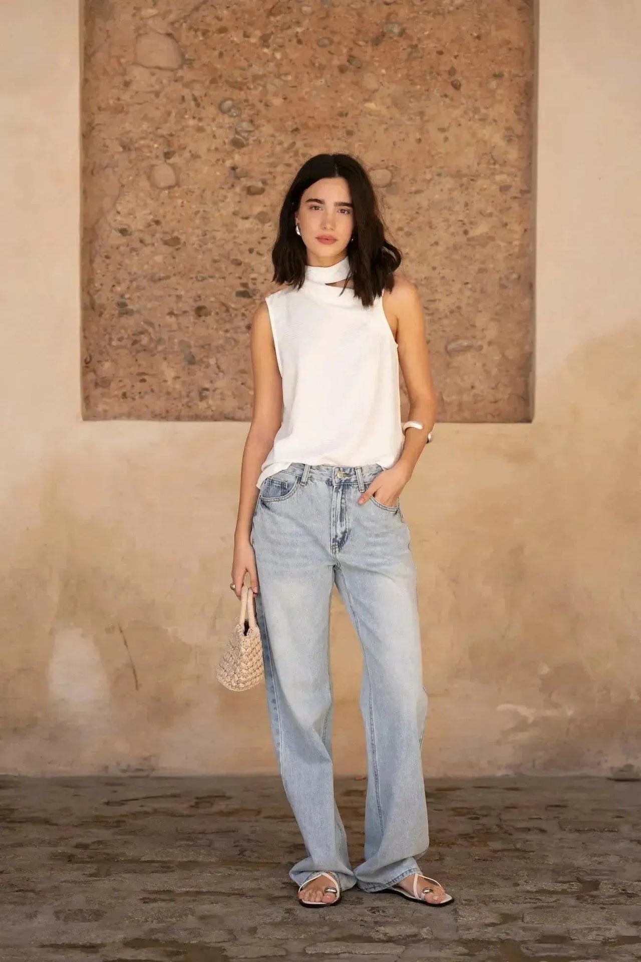 Modèle en blanc, posant devant un mur, vêtue d'un Jean Jambe Large à la Coupe Flatteuse, un choix parfait pour le jean jambe large femme.