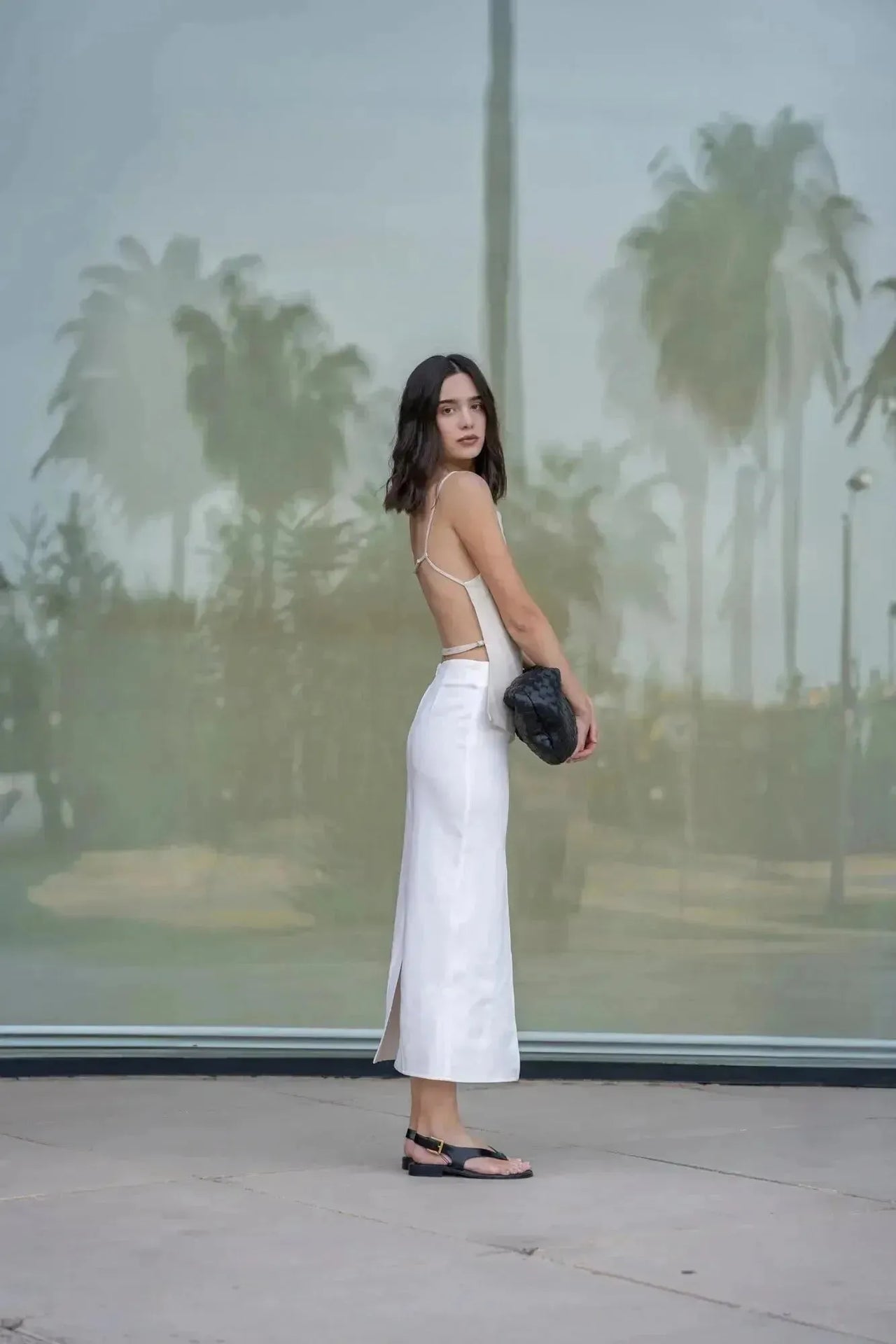 Femme de dos dans une jupe blanche longue femme, tenant un sac à main, ajoutant une touche de sophistication.