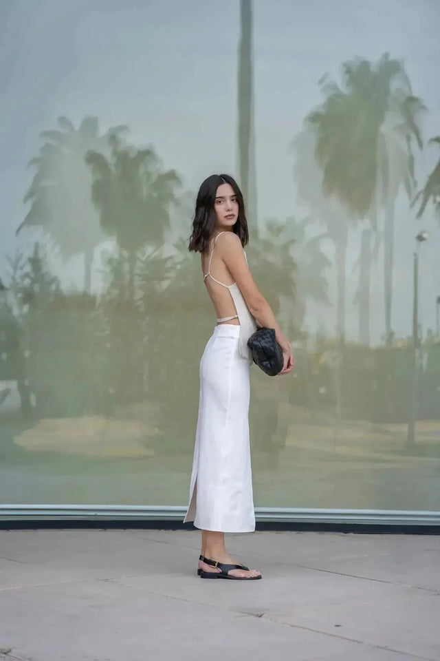 Femme de dos dans une jupe blanche longue femme, tenant un sac à main, ajoutant une touche de sophistication.